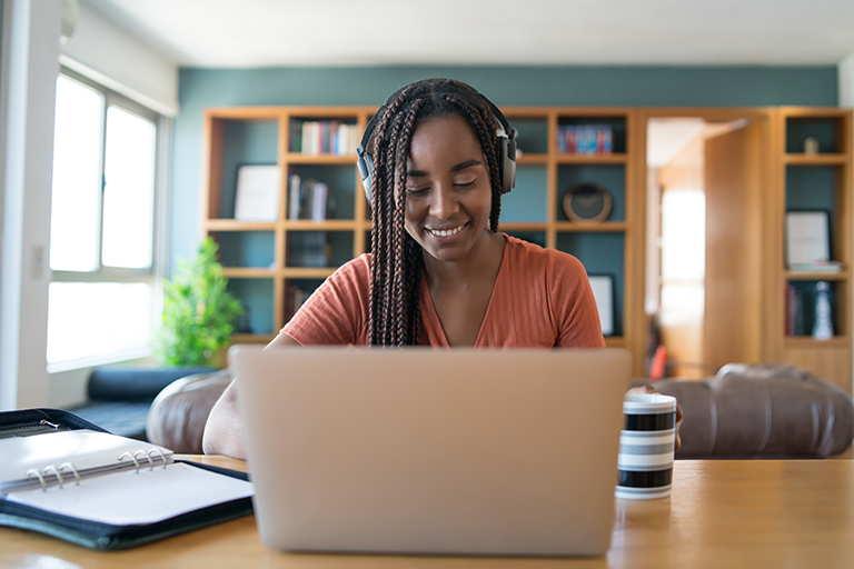 Woman working from home on laptop. Wearing headphones.